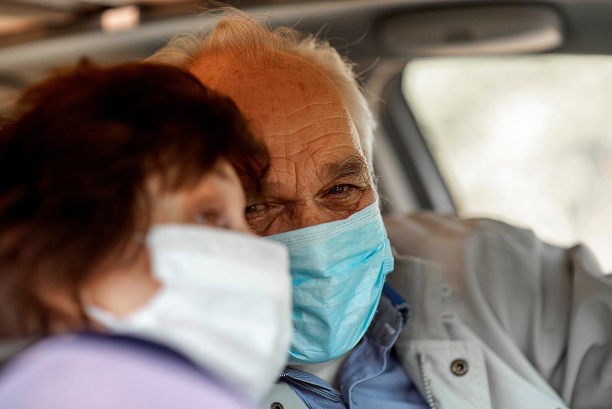 An elderly man in a medical face mask driving a car